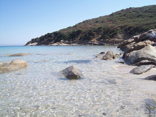 Una barca ancorata nelle acque trasparenti di Cala Zafferano con le montagne del Sulcis sullo sfondo spiagge militari teulada cala zafferano, porto tramatzu, is arenas biancas, poligono militare teulada