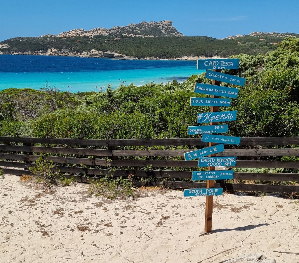 Beautiful Sardinian beach with a directional signpost pointing to global landmarks.