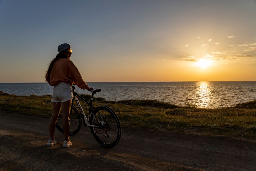 Woman with bicycle watching ocean sunset, creating a serene and adventurous atmosphere.