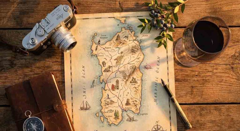 Una mappa stilizzata della Sardegna poggiata su un vecchio tavolo di legno, circondata da una macchina fotografica analogica, un rametto di mirto e un bicchiere di Cannonau. La luce è calda e dorata (Golden Hour). Stile "Travel Flatlay" professionale e invitante